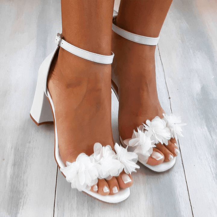 Women's elegant white block heel sandals with intricate floral accents, peep toe, & chic ankle strap for summer.