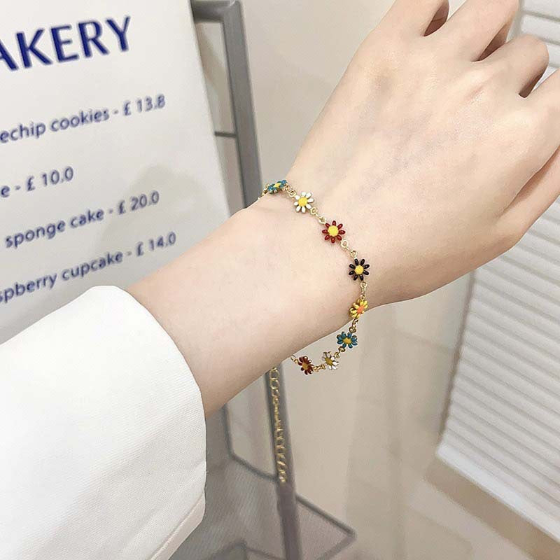 Close-up of a women's daisy charm bracelet featuring delicate white and yellow floral designs.