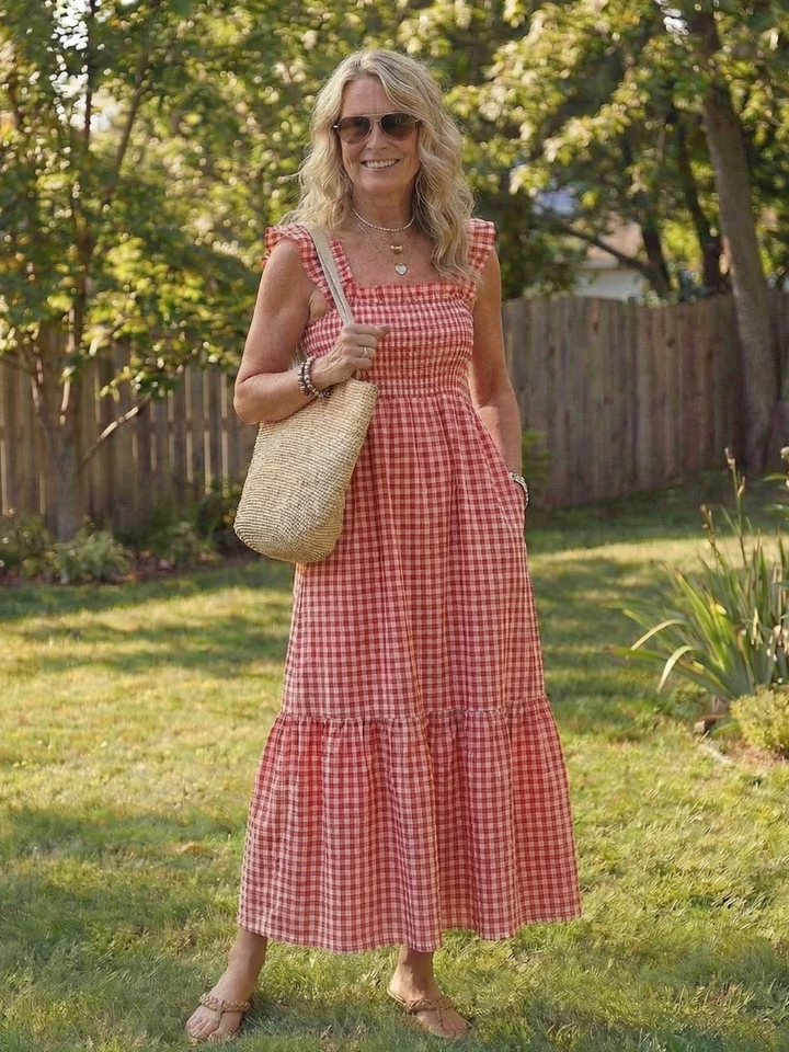 Detailed shot of a women's smocked gingham maxi dress, featuring flutter sleeves, square neck & tiered design.