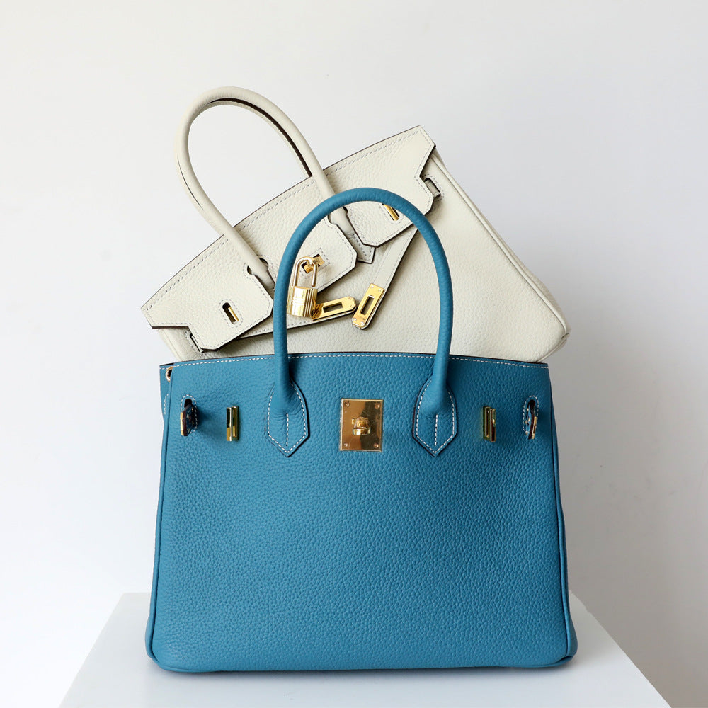 Women's luxury genuine leather shoulder bag, held by hand, emphasizing comfortable carry.