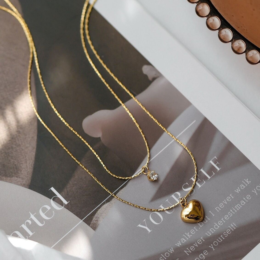 Elegant gold-tone layered necklace with a polished heart charm & a brilliant crystal pendant for women.