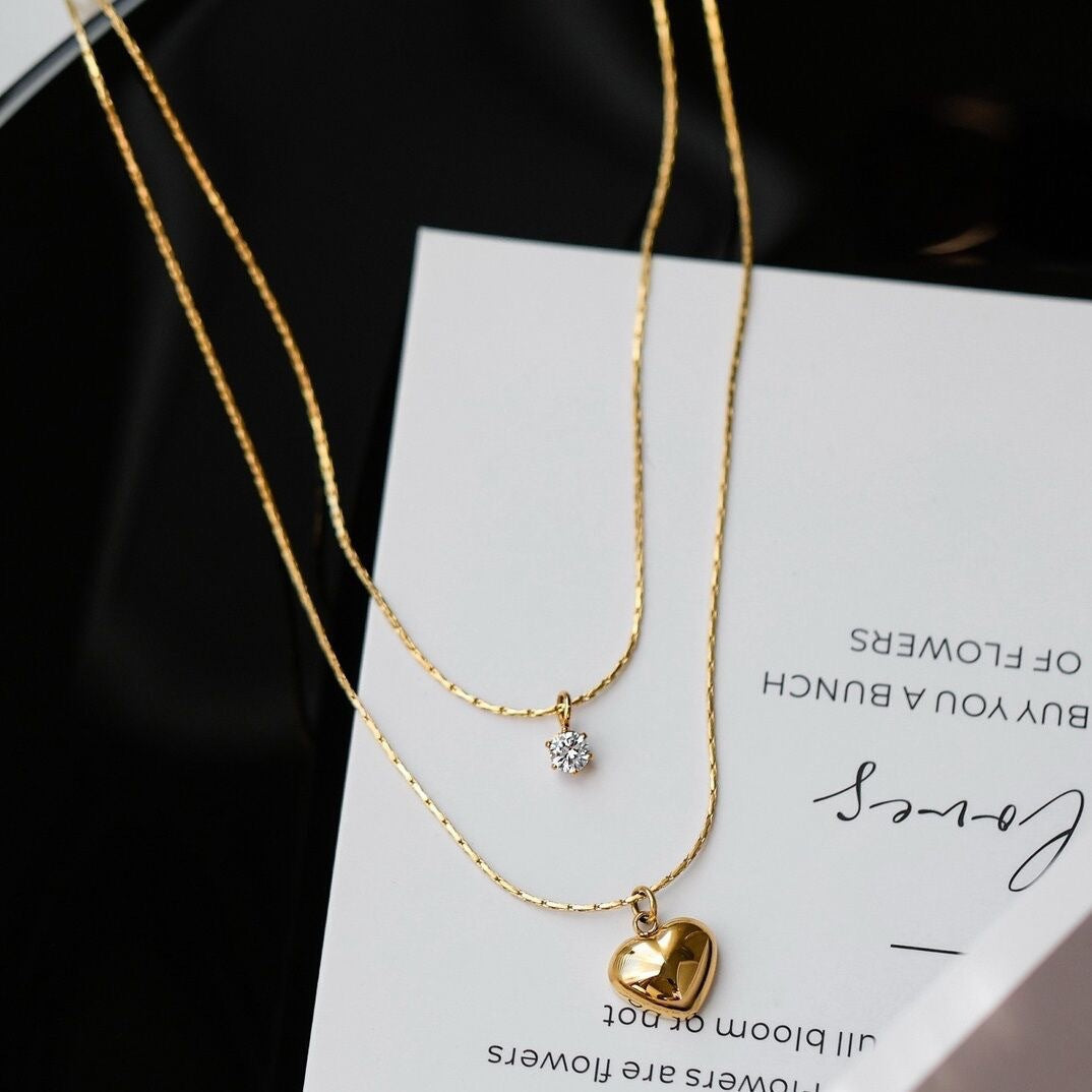 Fashionable women's gold layered necklace, featuring a delicate heart charm & a radiant crystal pendant.