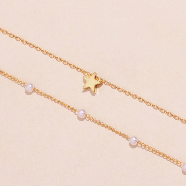 Gold plated layered necklace for women, adorned with radiant pearl charms and shimmering star pendants. Stylish accessory.
