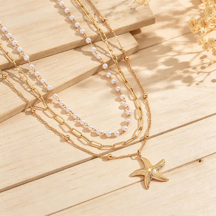 Shiny gold plated layered necklace showcasing a starfish charm & small pearl, perfect for beach outfits & summer.