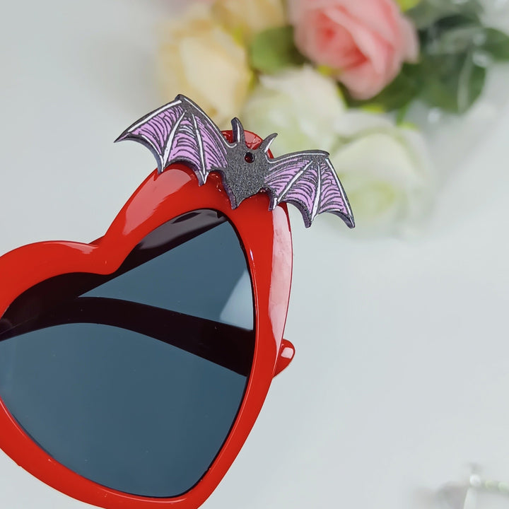 Unique women's heart sunglasses with intricate bat accents, a statement piece for any outfit.