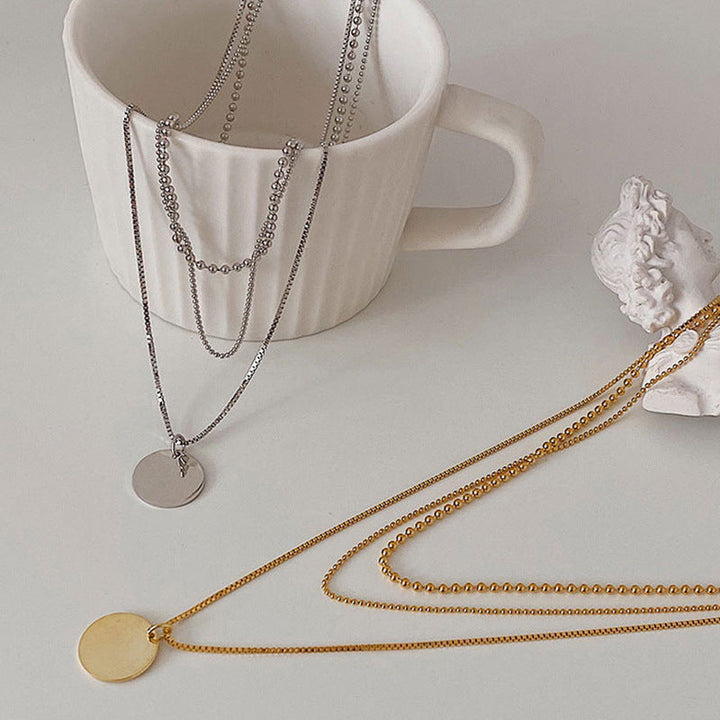 Close-up of a women's layered dainty necklace with delicate chains & small round pendants, highlighting its elegant design.