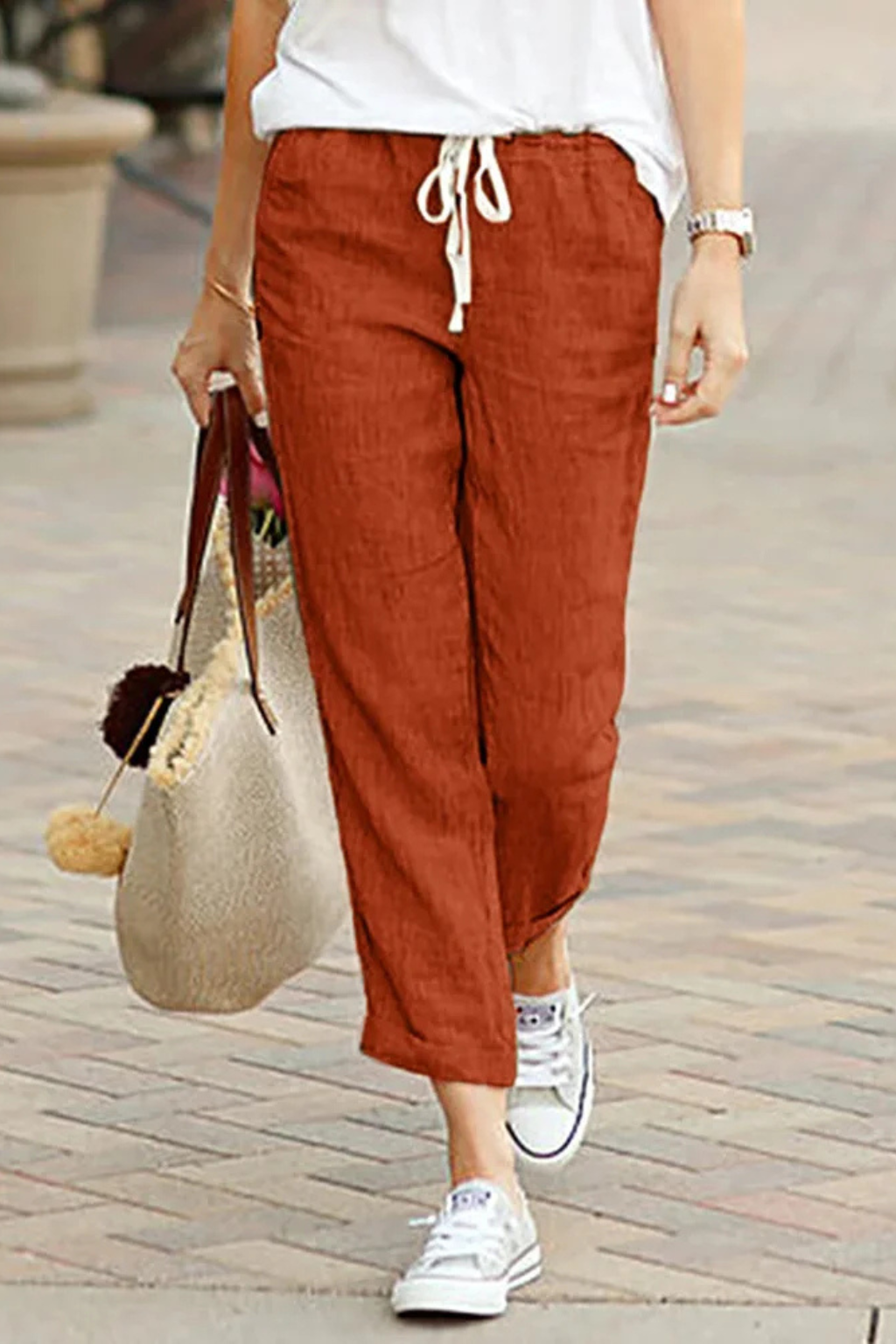 Woman wearing light women's cropped linen trousers with drawstring waist, walking outdoors on a sunny day.