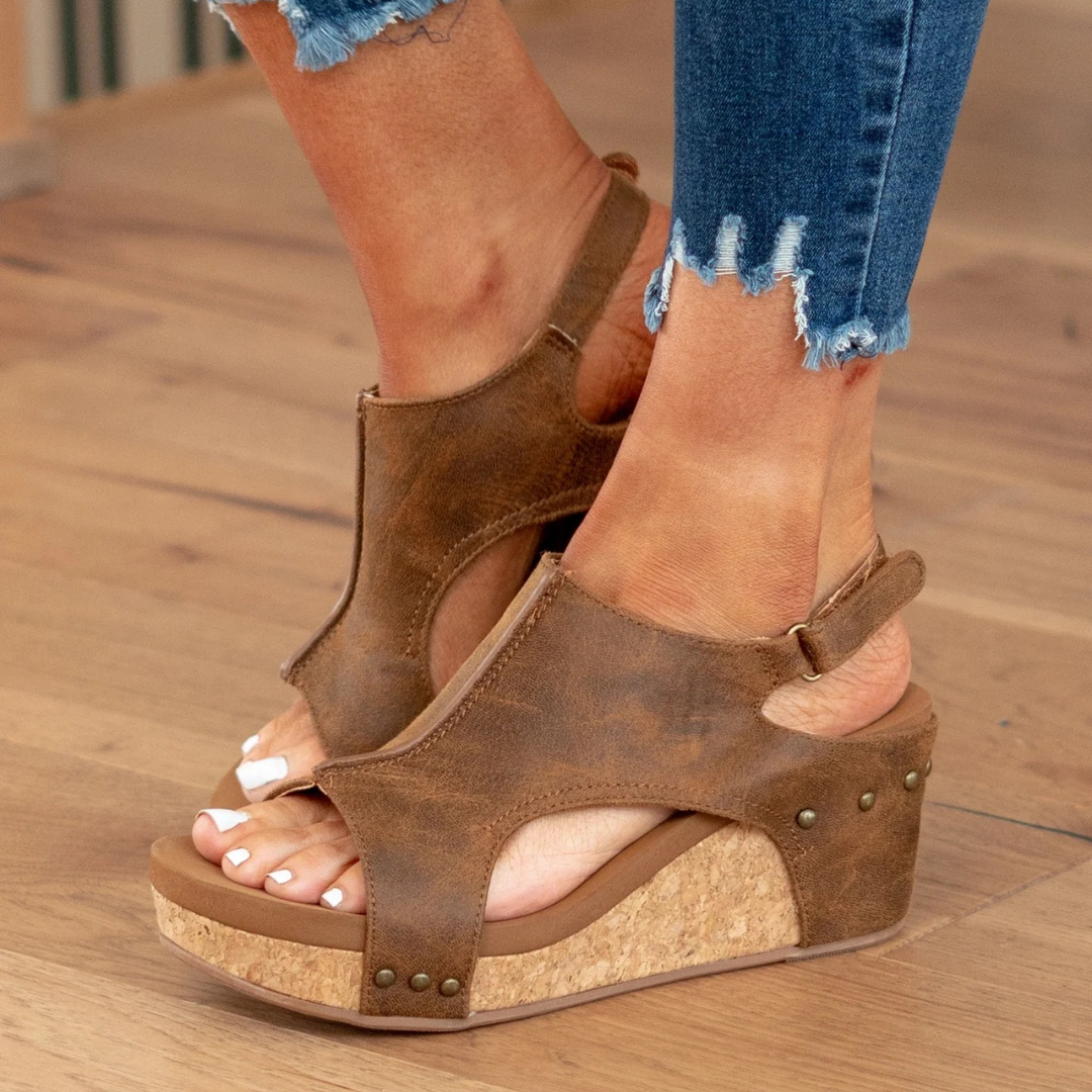 Woman wearing comfortable orthopedic studded wedge sandals. Stylish summer footwear with arch support.