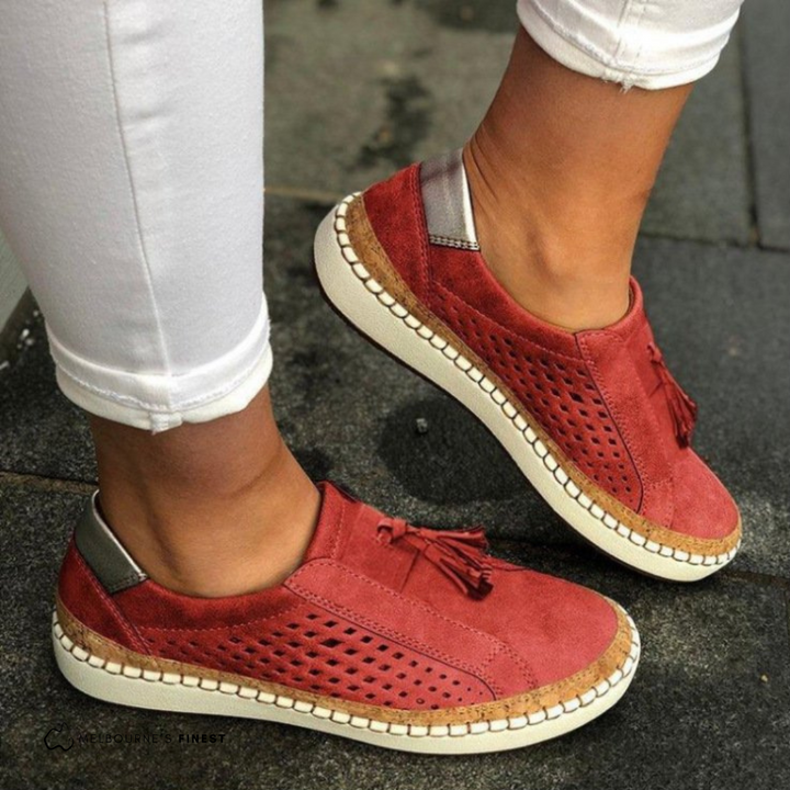 Womens perforated vegan leather slip-on flats with decorative tassels. Stylish and comfortable everyday footwear.