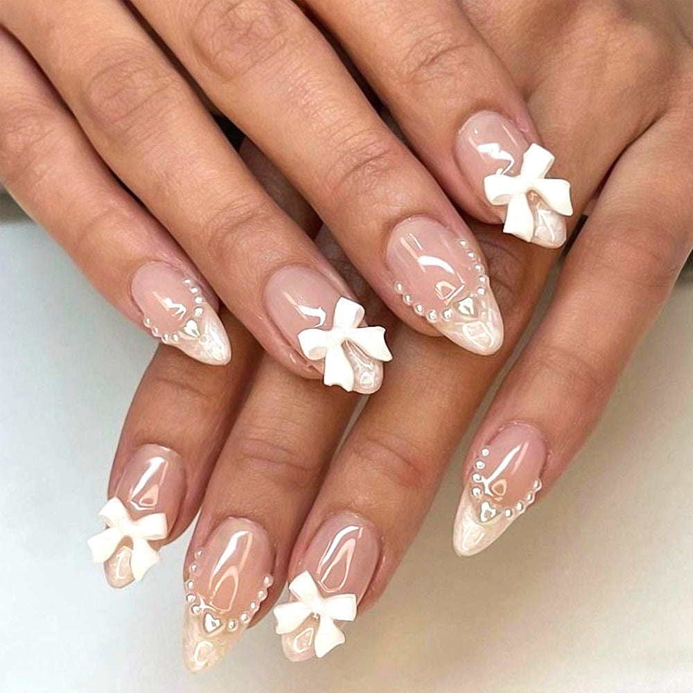 Women's pink press-on nail tips with delicate 3D bow and gem decorations for a quick, stylish manicure at home.