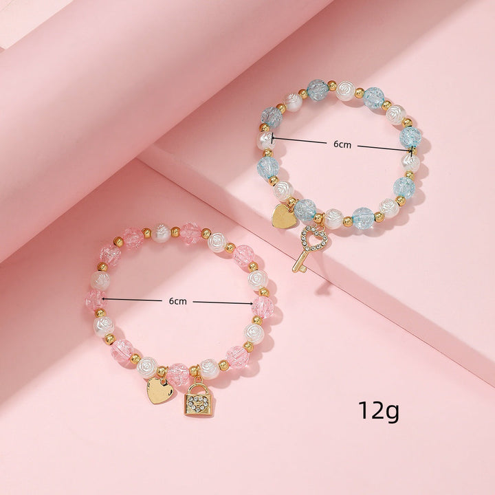 Close-up of a women's charm bracelet set featuring delicate heart & key charms on pastel beads. Elegant fashion.
