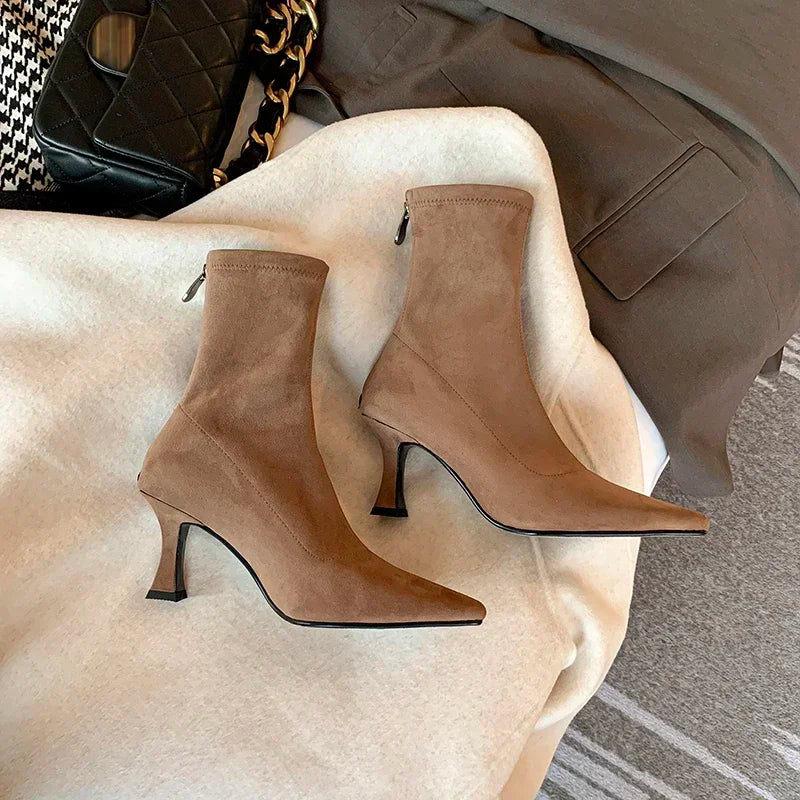 Woman wearing sleek black pointed toe sock boots with a kitten heel. Comfortable & chic ankle boots for elegant style.