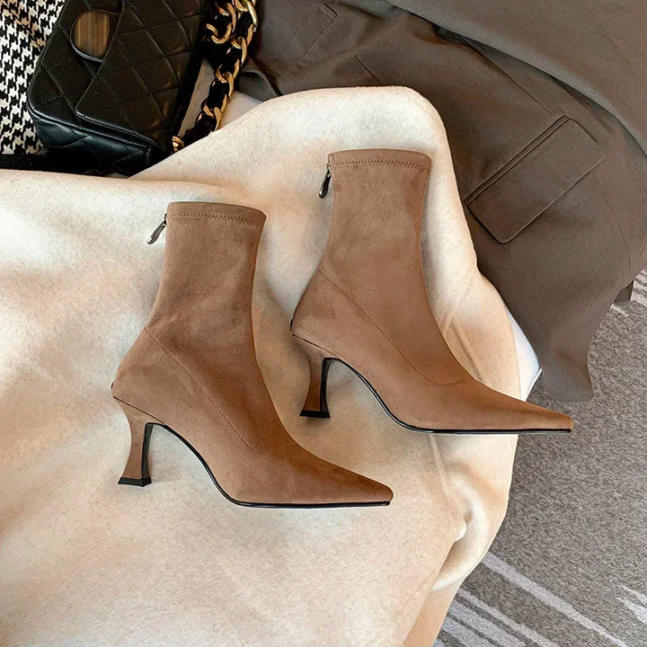 Woman wearing sleek black pointed toe sock boots with a kitten heel. Comfortable & chic ankle boots for elegant style.