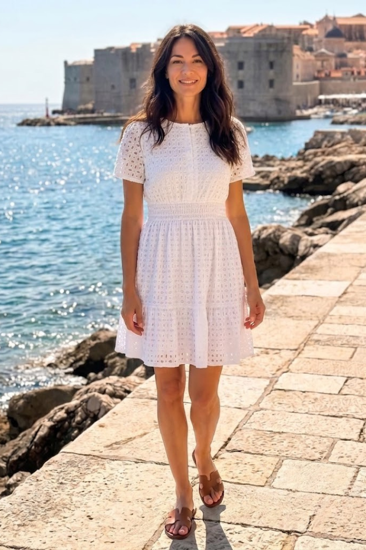 Woman wearing a white flutter sleeve eyelet mini dress, showcasing lightweight summer fashion & casual style.