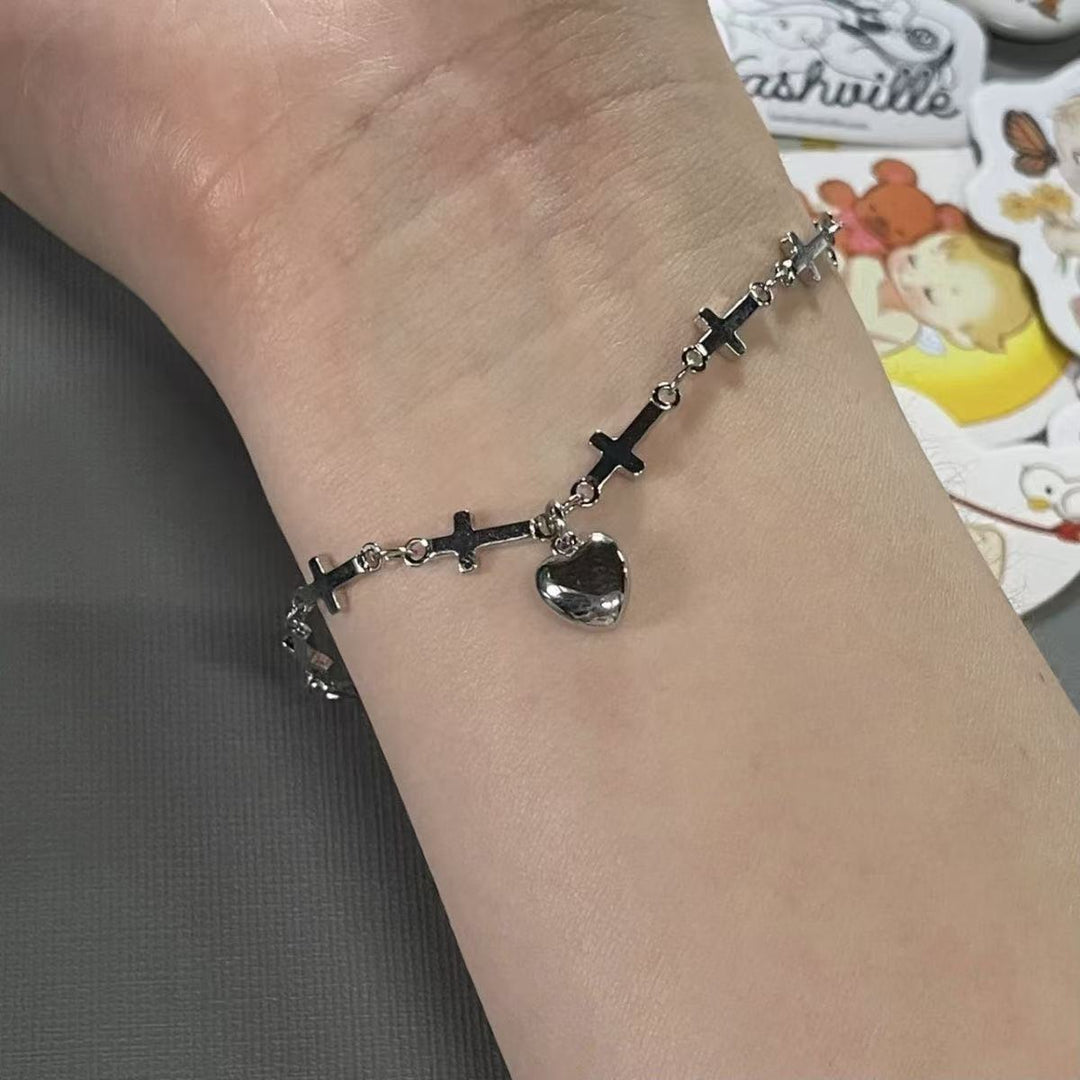 Women's silver charm bracelet with delicate cross and heart pendants, adjustable for a perfect fit, elegant fashion accessory.