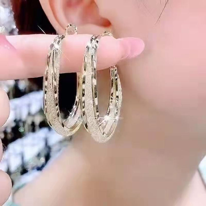 Gold-tone twisted oval hoop earrings for women, adorned with shimmering crystals. Stylish and elegant jewelry.