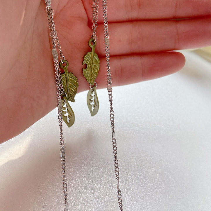 Gold-tone women's eyewear holder chain, a chic spectacle accessory with delicate green leaf motif design.