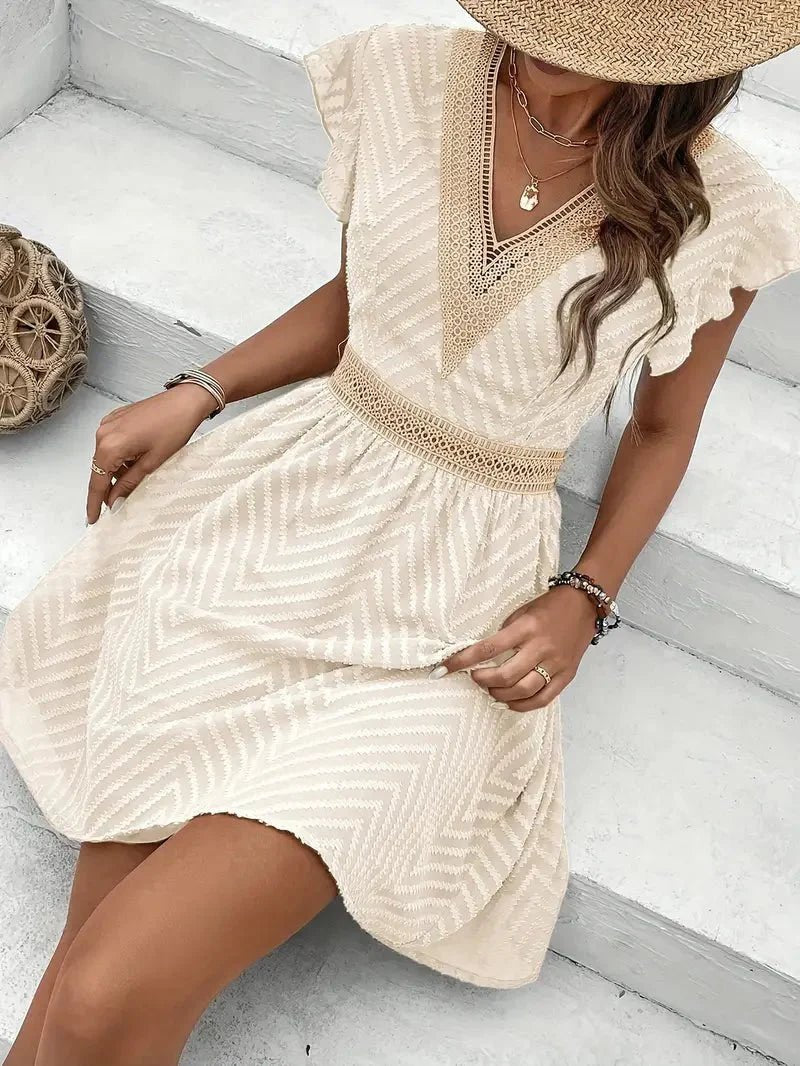 Boho style V-neck mini dress with lace trim, cap sleeves, and a flared hem. Warm weather fashion.