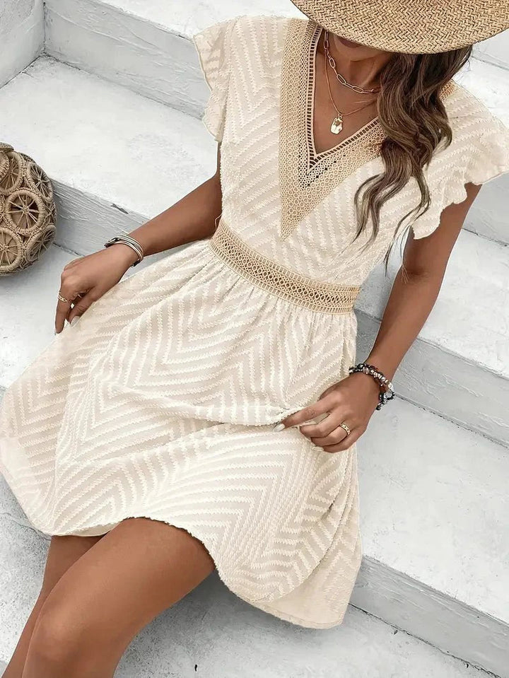Boho style V-neck mini dress with lace trim, cap sleeves, and a flared hem. Warm weather fashion.